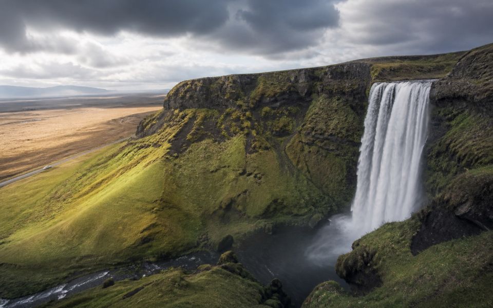 A waterfall, volcanic landscape, and a road among green rocks in Iceland