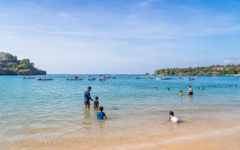 Families swim in the calm turquoise waters of the wide Jimbaran Bay