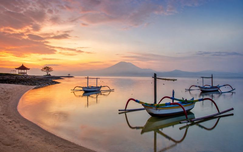 Traditional jukung boats and the silhouette of Mount Agung at sunrise in Sanur