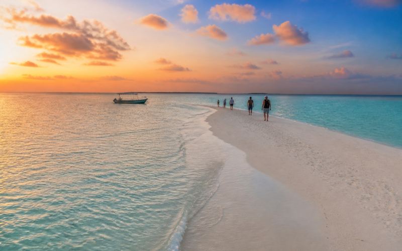Travelers walk along a narrow sandbar near Ukulhas at sunset