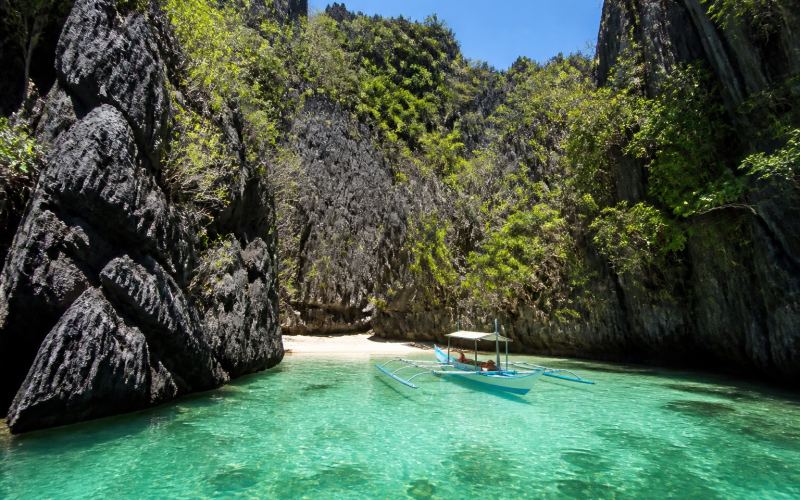 A hidden lagoon with a boat among the limestone walls of the El Nido archipelago