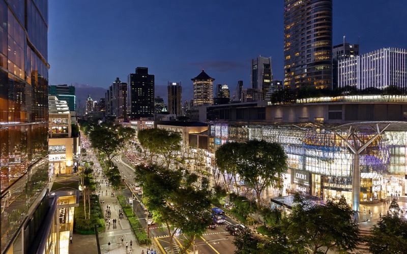 Подсвеченная Orchard Road вечером с пешеходами и тропическими деревьями