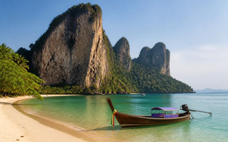 Limestone cliffs, a sandy beach, and a traditional boat at Railay Beach in Krabi